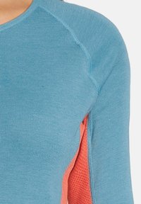 Maglia a maniche lunghe realizzata in un tessuto a maglia blu con un pannello in rete corallo sul lato. Scollatura rotonda e dettagli con cuciture a contrasto.