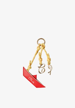 Porte-clés en cuir rouge avec cordons noués jaunes et breloques lettres dorées "C" et "T" attachées à un anneau porte-clés doré.