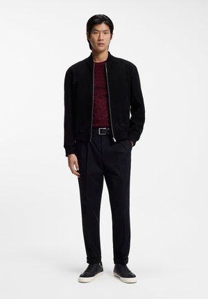 Black suede bomber jacket over a textured maroon sweater, paired with black trousers and black leather sneakers with white soles.