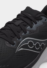 Μαύρο αθλητικό παπούτσι με μαύρα κορδόνια, γκρι λεπτομέρειες και ασημένιο κυματιστό λογότυπο στο πλάι πάνω από λευκή σόλα.