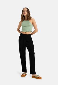 Top corto a righe verde chiaro con scollatura a halter e orlo a scalloped abbinato a pantaloni neri a vestibilità ampia e sandali platform marroni con cinturini verdi.