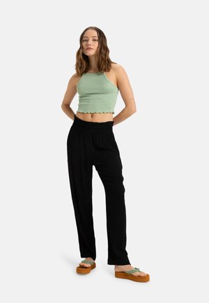 Top corto a righe verde chiaro con scollatura a halter e orlo a scalloped abbinato a pantaloni neri a vestibilità ampia e sandali platform marroni con cinturini verdi.