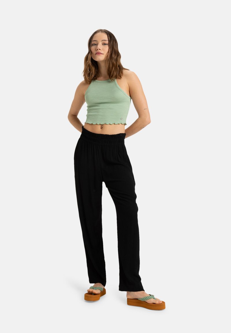 Top corto a righe verde chiaro con scollatura a halter e orlo a scalloped abbinato a pantaloni neri a vestibilità ampia e sandali platform marroni con cinturini verdi.