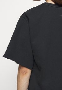 Musta ylisuurta t-paita, jossa on pyöreä pääntie, raakapäättelysleevejä ja pehmeä puuvillakudos. Ei näkyvää brändäystä tai kuvioita.