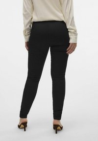 Sorte skinny bukser laget av et jevnt, elastisk stoff og med anklelengde. Brukt sammen med en lysfarget bluse og brune hæler.