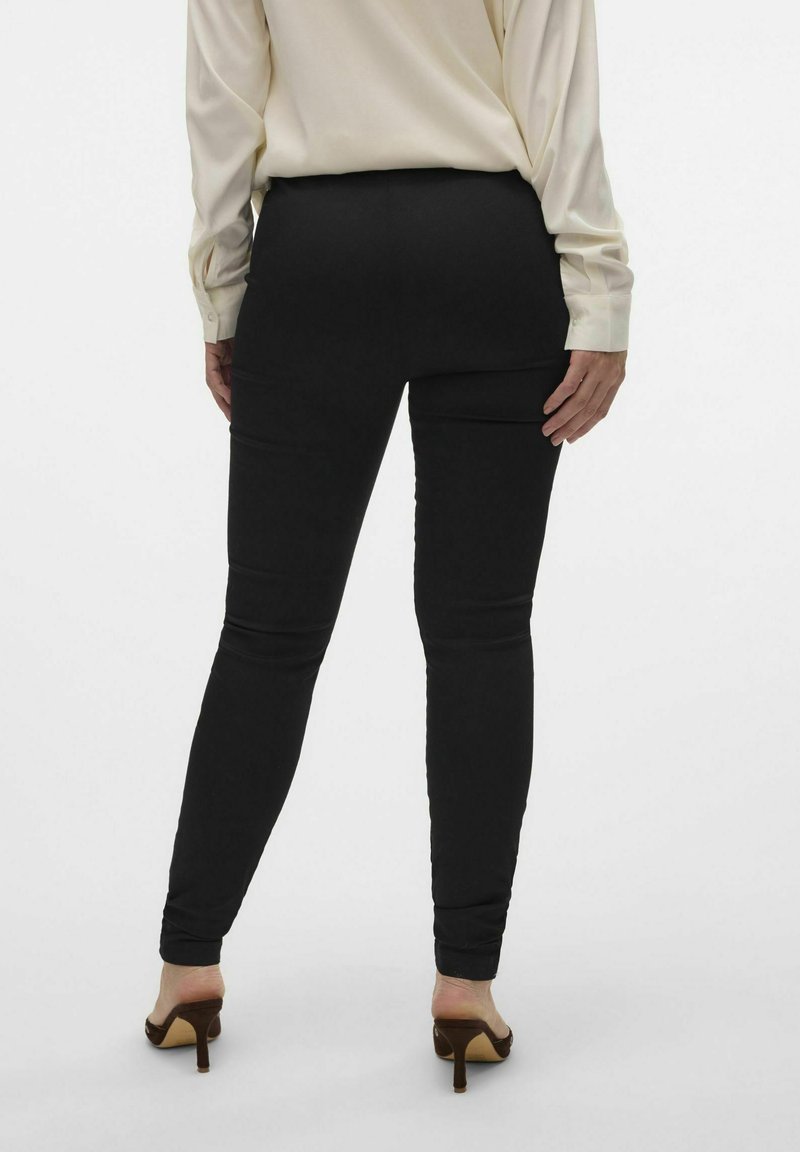 Czarne rurki wykonane z gładkiego, elastycznego materiału i o długości sięgającej kostki. Noszone z jasnym bluzką i brązowymi butami na obcasie.