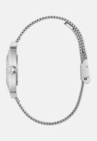 Srebrny zegarek z prostokątną kopertą i kamiennymi zdobieniami. Posiada teksturowaną metalową bransoletę oraz zapięcie na klamrę.