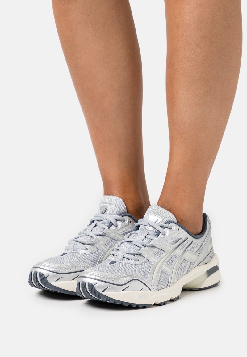 Jasnoszare buty sportowe z siateczkową cholewką i srebrnymi akcentami. Zaokrąglony nosek, sznurowadła, amortyzowana podeszwa i teksturowana podeszwa zewnętrzna zapewniająca przyczepność.