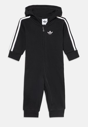 Crni dječji kombinezon s kapuljačom, prednjim patentnim zatvaračem, bijelim Adidas prugama na rukavima i Adidas logotipom na prsima. Dugi rukavi i nogavice.