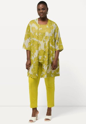Kimono floreale giallo e bianco, con una vestibilità ampia e maniche larghe, abbinato a pantaloni gialli coordinati. Tacchi bianchi aperti completano l'outfit.