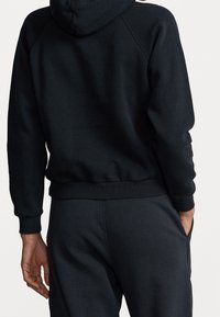 Svart bomullshuvtröja med en mjuk textur, som har huva, ribbade ärmslut och nederkant, i kombination med matchande joggers och en sidoficka.