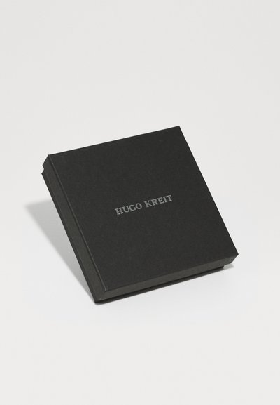 Caja cuadrada negra con acabado mate, que presenta el texto en relieve "HUGO KREIT" en plata. Diseño limpio y minimalista.