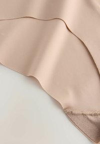 Tissu beige lisse avec bord festonné, présenté sur une surface claire, montrant texture et coutures en gros plan.