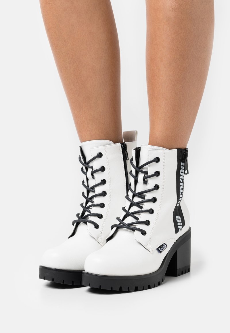 Vita fusk läder ankelskor med svarta snören, dragkedjedetaljer och texturerade svarta klackar. Har en robust sula och varumärkesdetaljer.