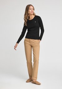 Svart bomullsskjorta med lång ärm och rund halsringning, kombinerad med beige bomullsbyxor och bruna mockasneakers. Minimalistisk design.