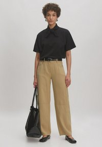 Zwarte korte mouwen shirt met een geknoopte kraag, beige wijde broek met zijzakken, zwarte platte schoenen en een zwarte totebag.