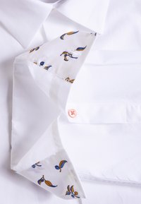 Witte overhemd met een contrasterend bloemenpatroon in blauw en geel op de binnenkraag en manchetten, met een roze knoop op de manchet.