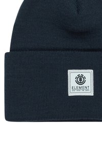 Berretto lavorato a maglia di colore blu scuro con risvolto. Presenta una toppa quadrata bianca con testo del logo e design circolare. Texture morbida e vestibilità aderente.