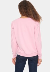 Sudadera de color rosa claro con mangas largas, cuello redondo y puños de canalé. Textura suave y corte holgado, combinada con jeans de color azul oscuro.