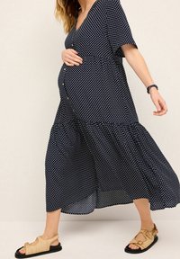 Navy sinipuneiden mekko v-aukolla, lyhyillä hihoilla ja kerroksellisella hameella. Yhdistetty vaaleanbeigeihin sandaaleihin, joissa on koristeellisia yksityiskohtia.