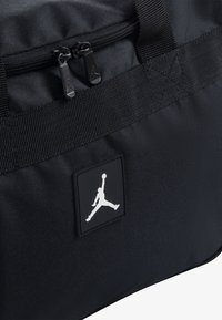 Black duffel bag featuring a smooth fabric surface, dual zipper closure, and a prominent white Jumpman logo on a square patch.