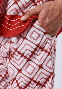 Rood en wit patroonkatoen met geometrische vormen. Close-up toont hand in de zak, waarbij de textuur en ontwerpdetails worden benadrukt.