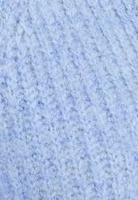 Tessuto lavorato a maglia di un blu chiaro, con una superficie texturizzata e leggermente pelosa, che presenta un motivo a trama allentata e sottili variazioni di colore.