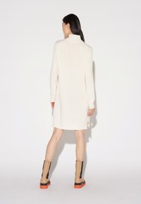 Abito maglione in bianco sporco con colletto alto, maniche lunghe e spacchi laterali, abbinato a stivaletti alla caviglia beige e neri con suole arancioni.