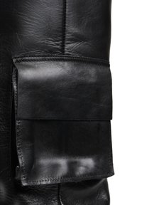 Czarna skórzana tkanina o teksturowanym wykończeniu, z prostokątną kieszenią naszywaną po boku, podkreślającą gładką powierzchnię i szwy.