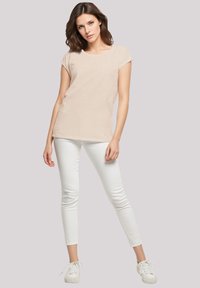 Beige short-sleeve top made of soft fabric, paired with white fitted pants and white sneakers, creating a clean, casual look.