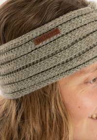 Bandeau en tricot en laine grise douce, présentant plusieurs bandes horizontales texturées et une étiquette en cuir marron avec "Knit Factory".