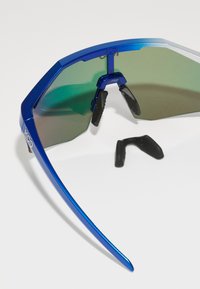 Blaue, winkelförmige Sonnenbrille mit grünen, verspiegelten Gläsern, Gummi-Nasenpads und schwarzen Bügelspitzen. Auffällige Markenkennzeichnung am Rahmen.