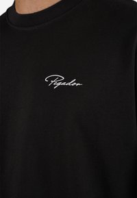 Black cotton t-shirt with a round neck, featuring white embroidered "Pegador" logo on the left chest area. Simple and minimalist design.