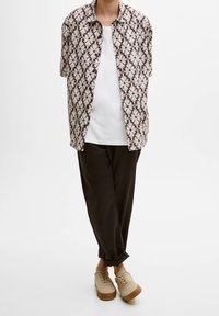 Koszula z krótkim rękawem w brązowo-kremowy wzór, zestawiona z białym t-shirtem, czarnymi spodniami i beżowymi butami sznurowanymi.