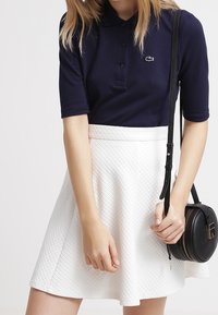 Mörkblå polo med korta ärmar och knäppning fram, kombinerad med en vit strukturerad skaterkjol. Tillbehören inkluderar en liten svart axelremsväska.