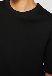 Černé bavlněné tričko s kulatým výstřihem, krátkými rukávy a hladkým povrchem, které má jednoduchý design bez vzorů nebo akcentů.