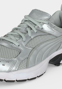 Ασημί και γκρι αθλητικό παπούτσι Puma για τρέξιμο με αεριζόμενο πάνω μέρος από διχτυωτό υλικό, επενδυμένο γιακά, κορδόνια και λευκή υφή σόλας με μαύρο πέλμα.