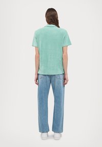 Polo shirt a maniche corte di colore verde menta con una texture morbida, abbinato a jeans in denim blu chiaro a gamba larga e sneakers bianche.