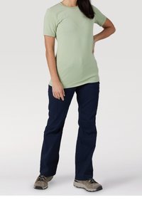 T-shirt verde chiaro a maniche corte abbinato a pantaloni cargo blu scuro, con tasche e vestibilità rilassata, indossato con scarpe da trekking grigio chiaro.