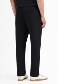 Zwarte broek van een gladde stof, met een rechte pijp, twee achterzakken en een discreet logo-detail nabij de tailleband.