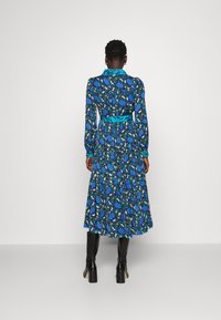 Abito midi floreale blu con maniche lunghe, vita con cintura e colletto. Presenta motivi di fiori neri e blu su uno sfondo scuro.