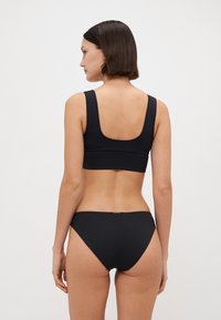 Fekete bikini szett, amelynek jellemzője a kerek nyakú bralette és az alacsony derekú alsó. Simaság és rugalmasság jellemzi, látható fém részek vagy minták nélkül.