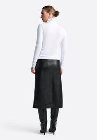 Valge pikad varrukad särk, millel on rippuv krae, koos musta nahast midi seeliku ja põlvekõrguste mustade saapatega, nähtav tagant.