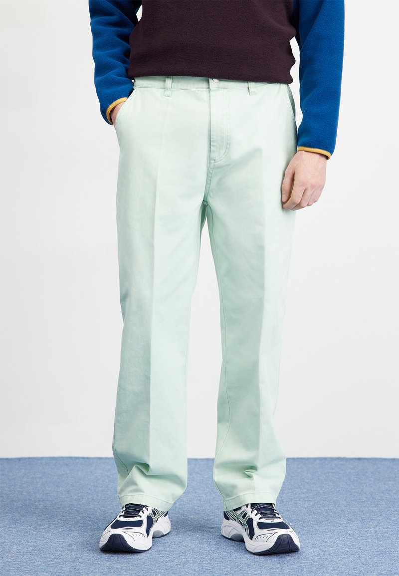 Light green, straight-leg trousers with a front pleat, made of cotton. Paired with navy and blue pullover and dark athletic shoes.