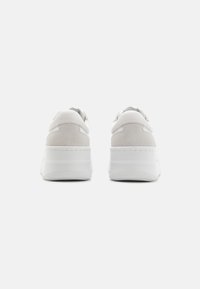 Plattformsneakers med en hvit glatt skinn- og semsket skinnoverdel, tykk hvit gummisåle og ingen synlige snørebånd.