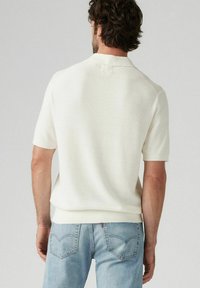 Vit kortärmad stickad polo med en strukturerad väv och ribbade detaljer vid kragen och nederkanten, i kombination med ljusblå jeans.