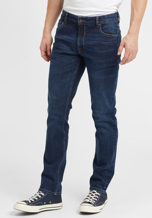 Mørkeblå denimjeans for menn, slim fit, femlommesdesign, synlige sømdetaljer, brukt med marineblå høye sneakers.