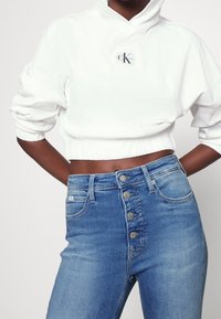 Vit kortärmad huvtröja med logotypdetalj. Höga blåjeans med knappgylf, fem fickor och lätt blekning i tyget.