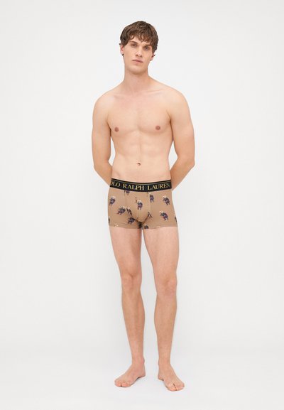 Bruine boxershorts met een herhaald bloemmotief, zwarte tailleband met "POLO RALPH LAUREN" in gouden letters, gladde stoftextuur.