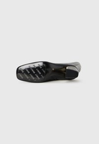Stivaletto nero con tacco sdraiato su un lato che mostra la suola con marchio e il motivo ripetuto del testo "DKNY", con design a punta squadrata.